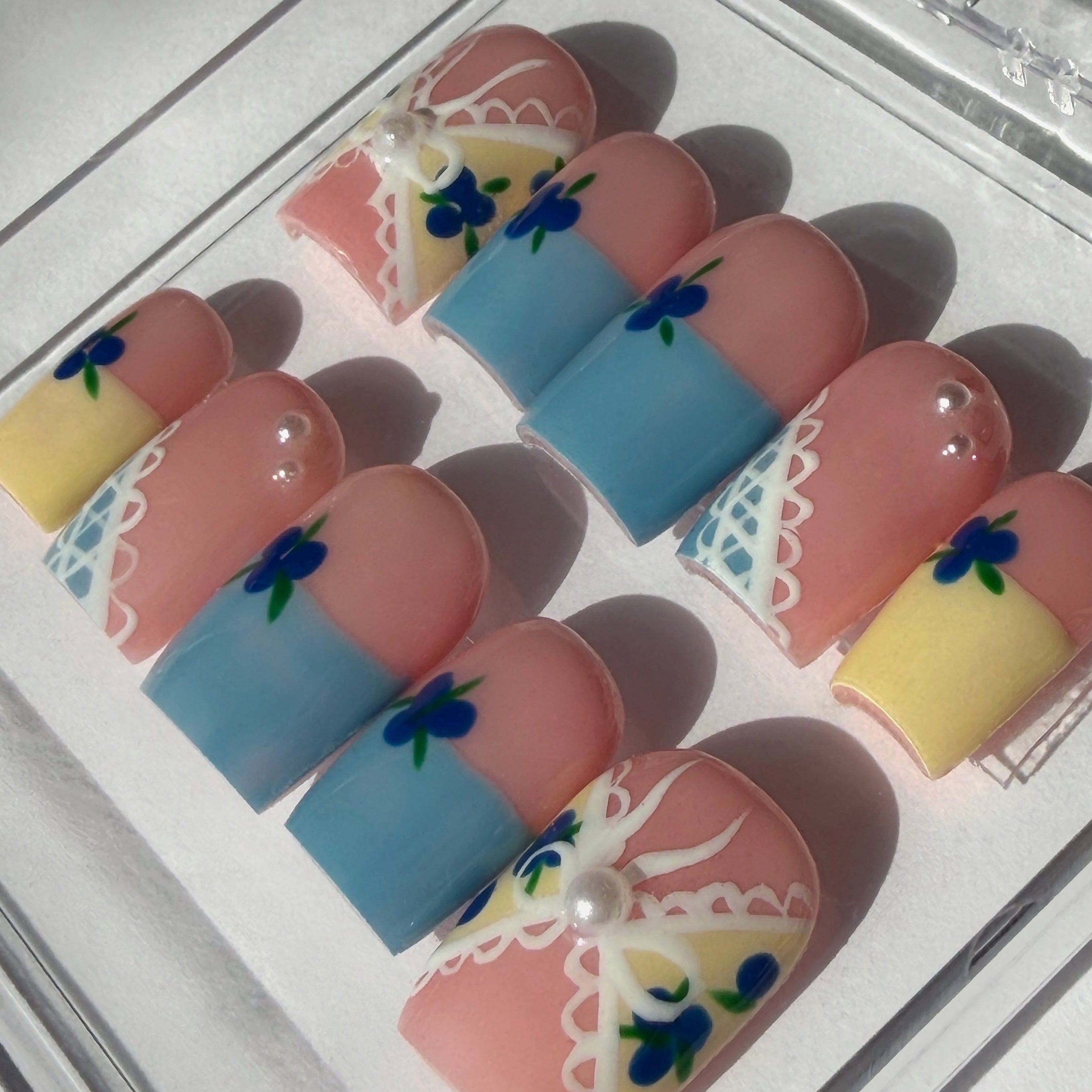 Set of decorative false nails with blue, pink, and yellow designs on a white background.