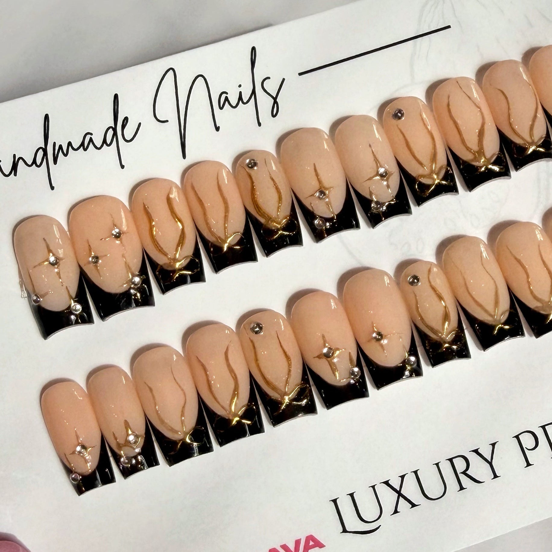 Luxury black French tip press-on nails with gold accents on a branded paper