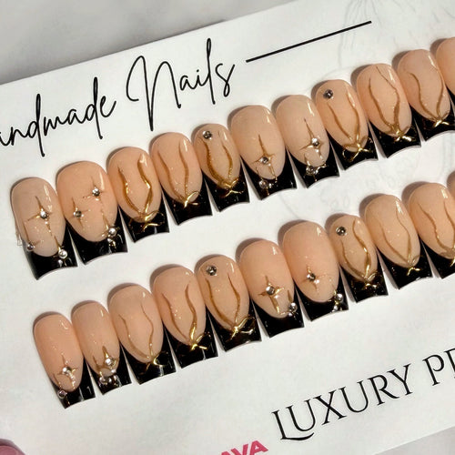 Luxury black French tip press-on nails with gold accents on a branded paper
