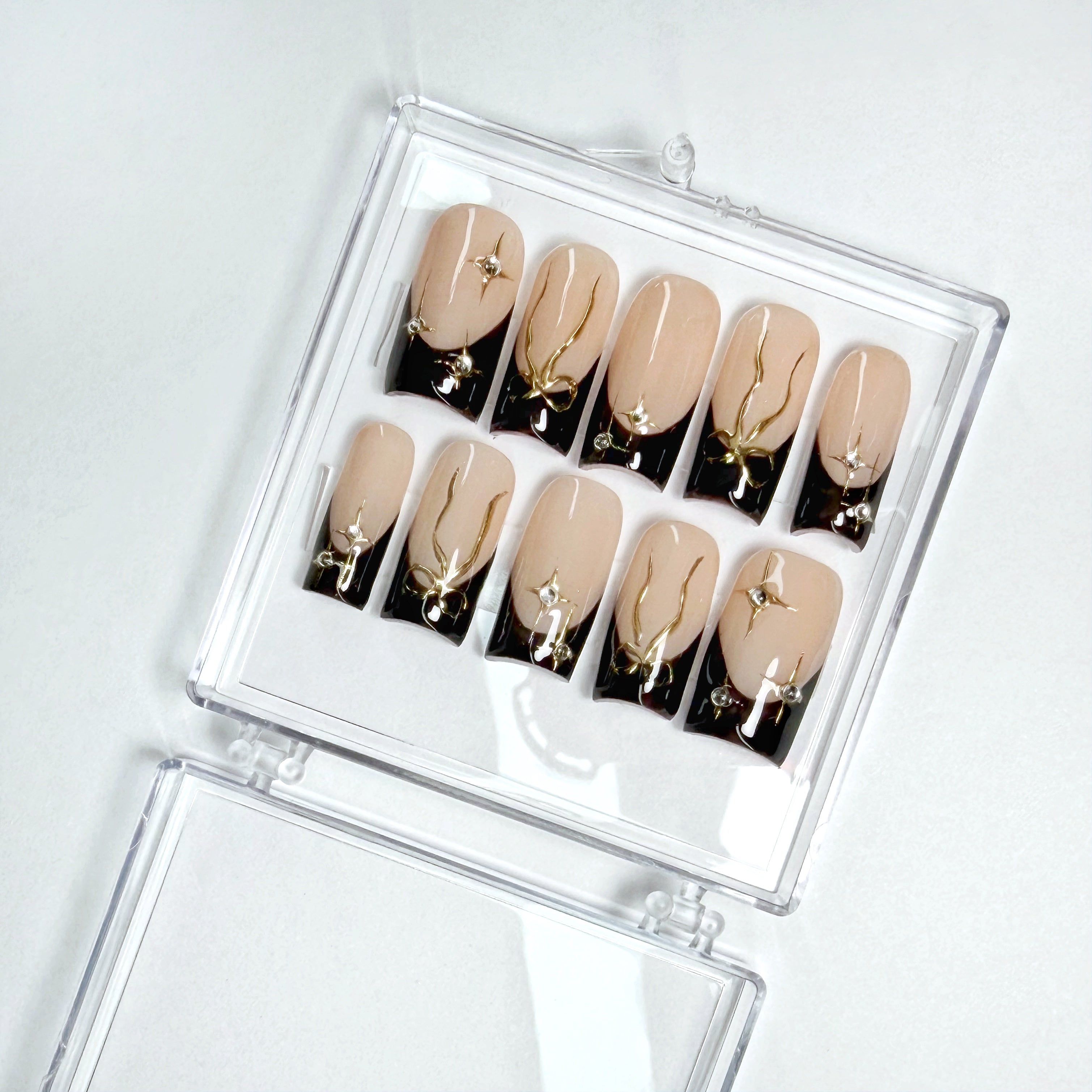 Set of beige and black nail art designs in a clear case on a white background