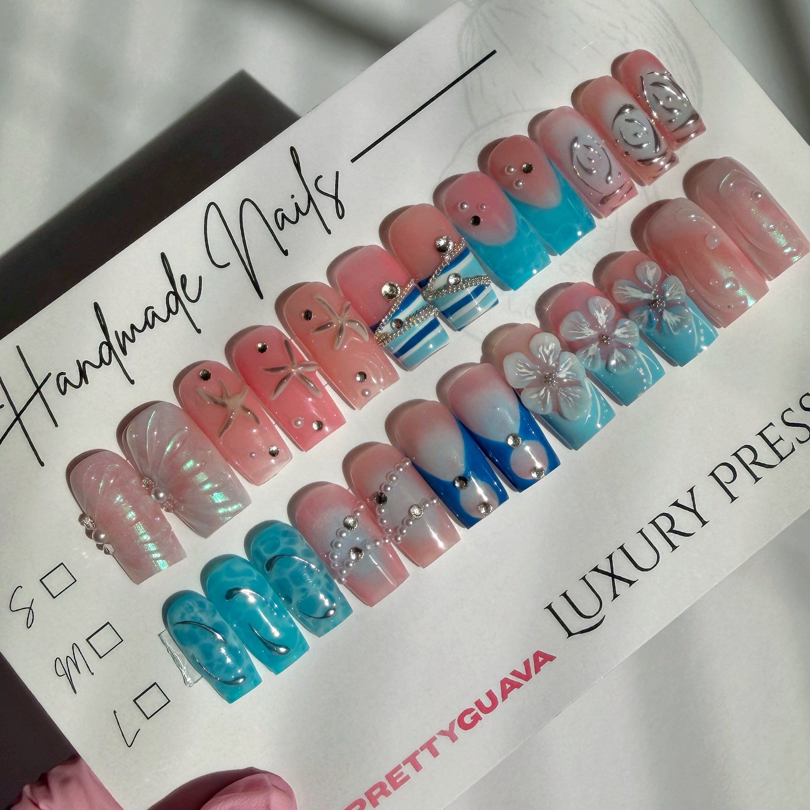 24 pcs set of pink and blue press-on nails with decorative elements on a PrettyGuava branded paper.