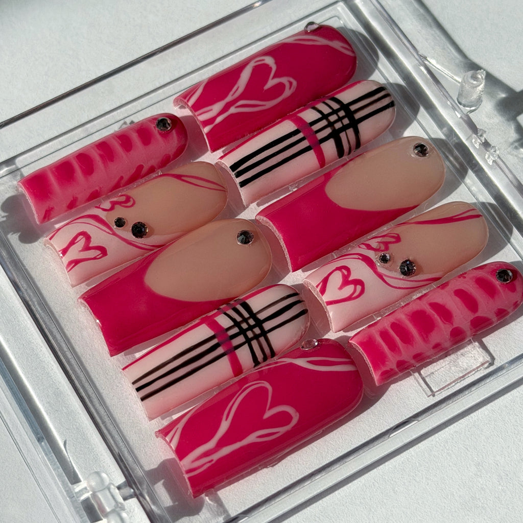 Set of pink and beige nails with decorative patterns in a clear case on a white background.