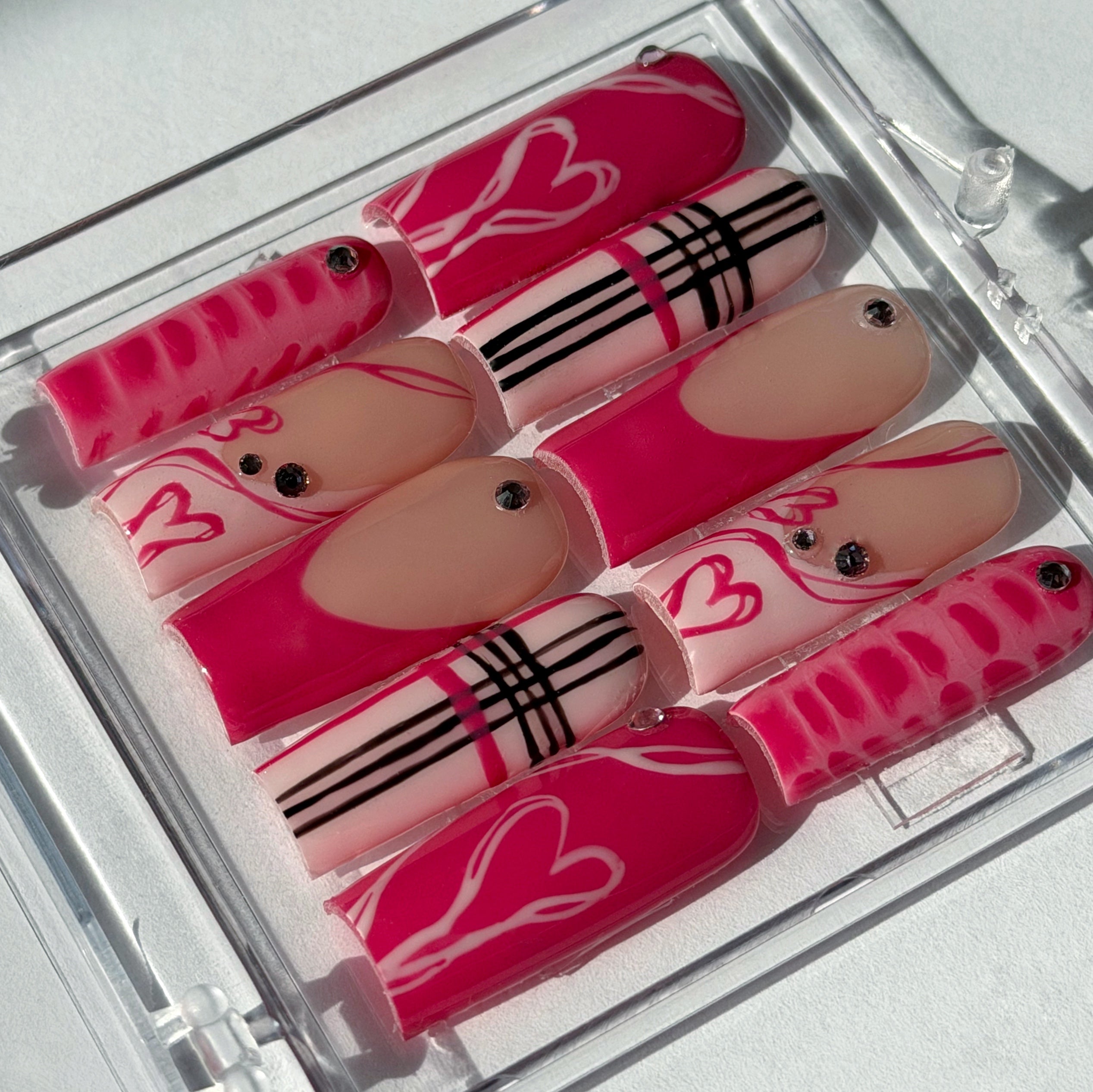 Set of pink and beige nails with decorative patterns in a clear case on a white background.
