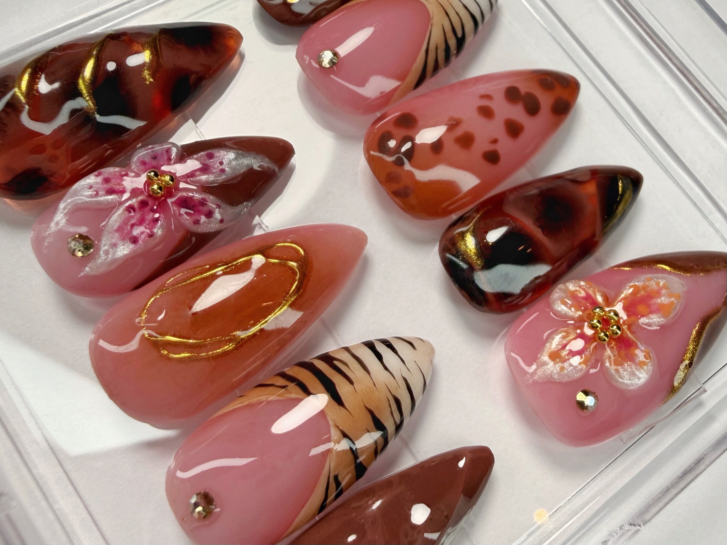 Set of decorative false nails with various patterns including flowers and animal prints in a clear case on a white background.