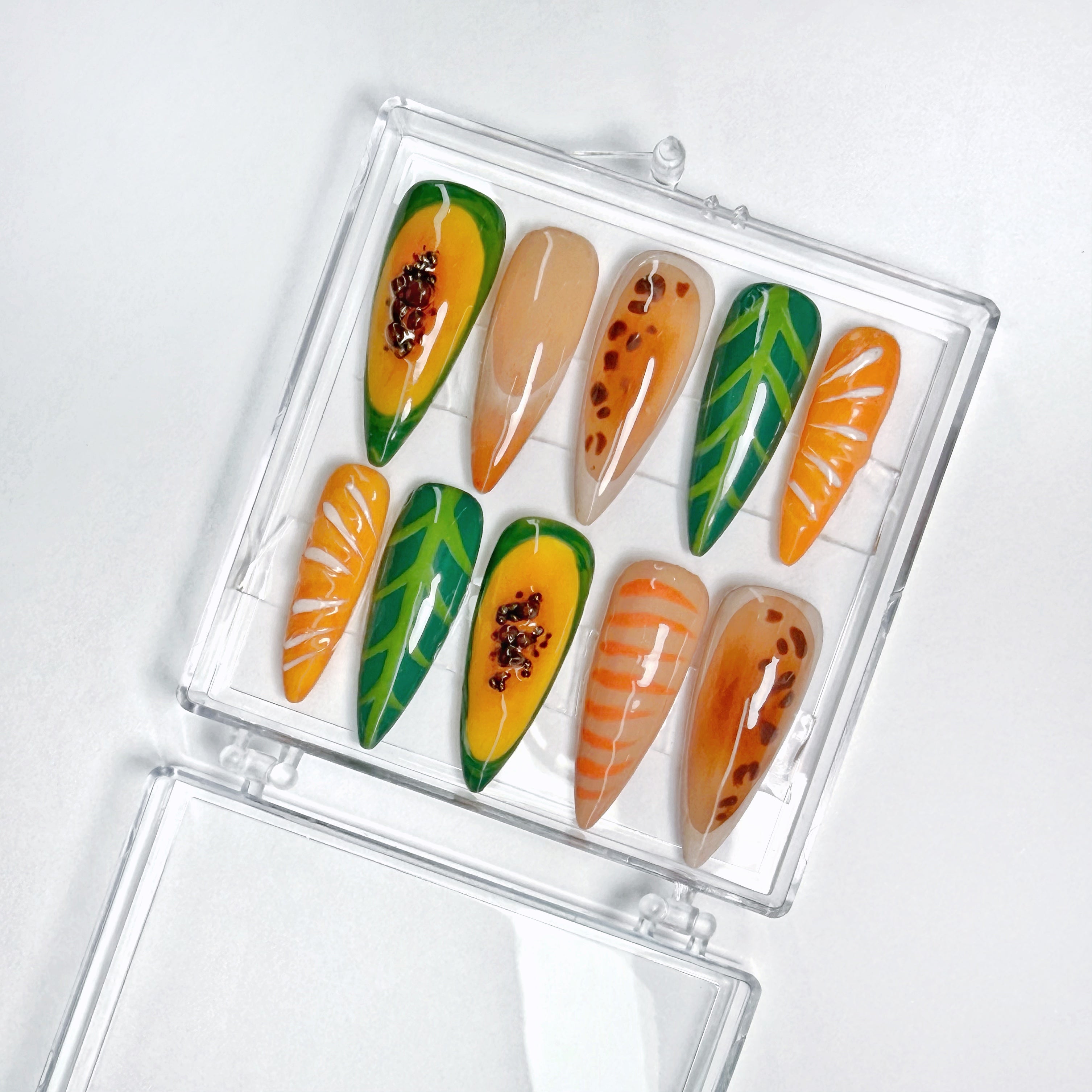 Set of nail art designs resembling a papaya with leaf patterns in a clear case on a white background