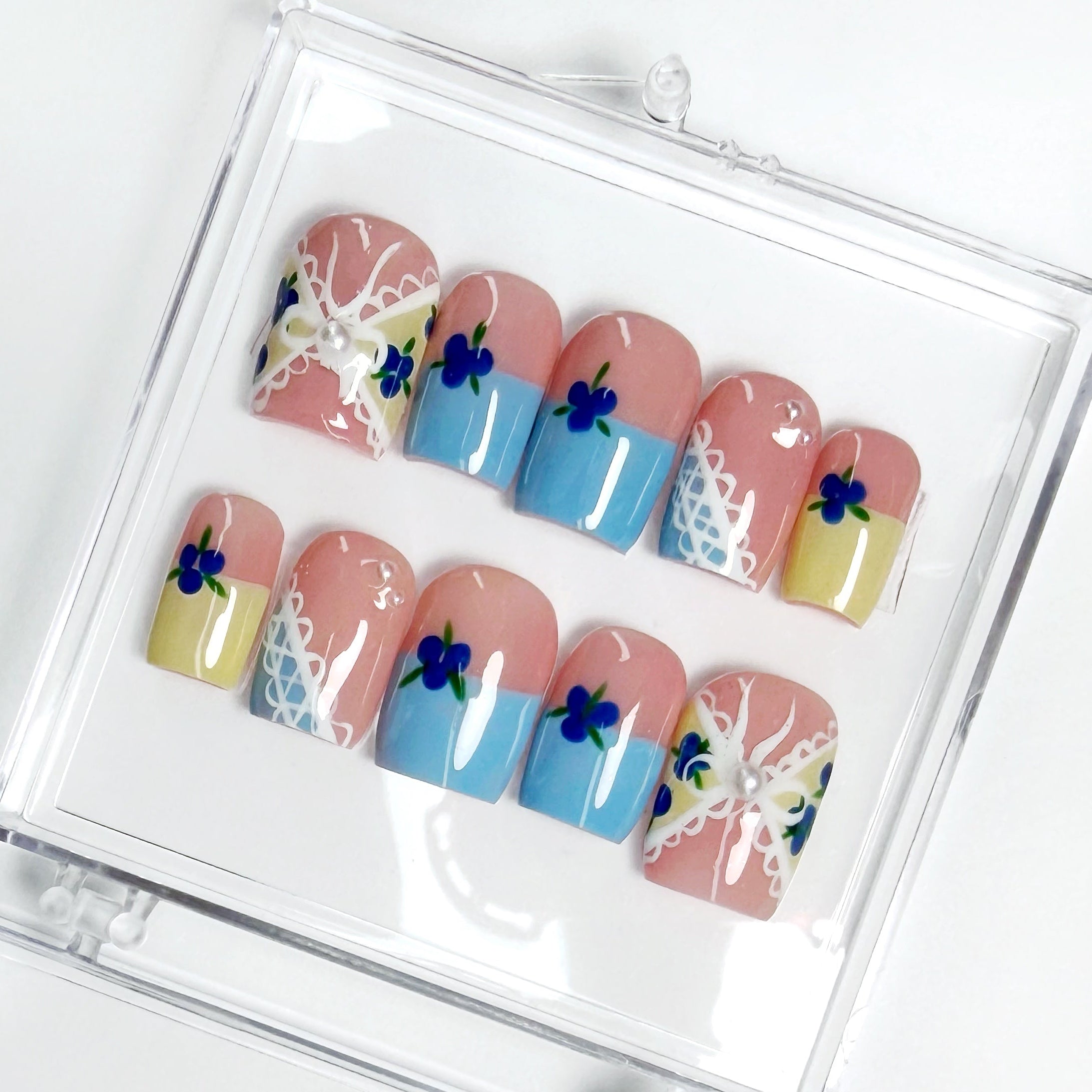 Set of nails with blueberry themed art designs in a clear display case on a white background