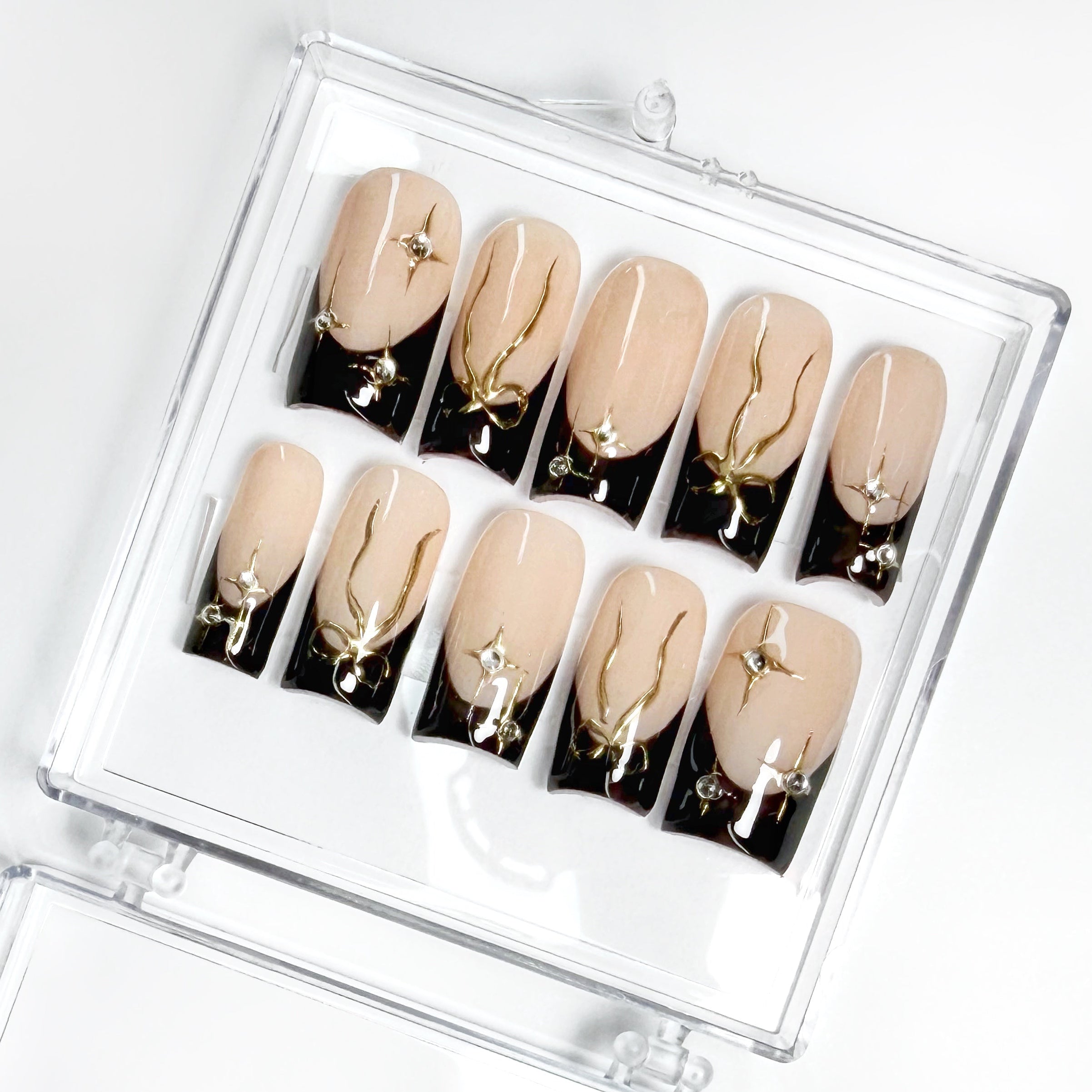 Set of beige and black nail art designs in a clear case on a white background