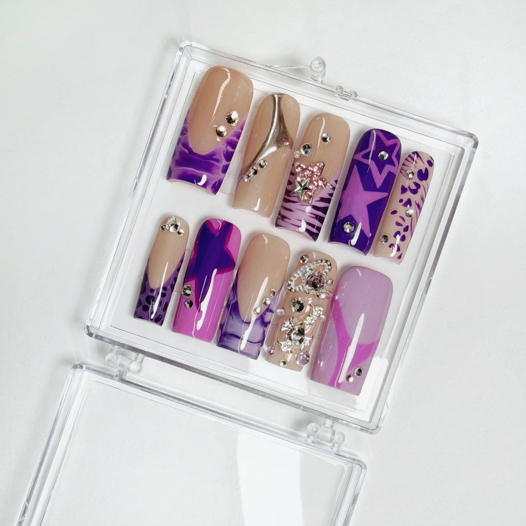 Set of purple and beige nail designs with rhinestones in a clear case on a white background