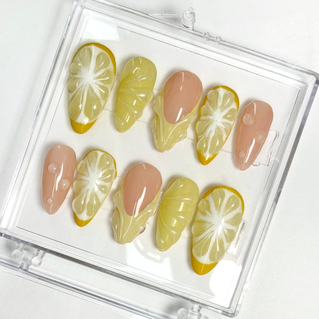 Set of press-on nails with lemon and yellow design in a clear case on a white background