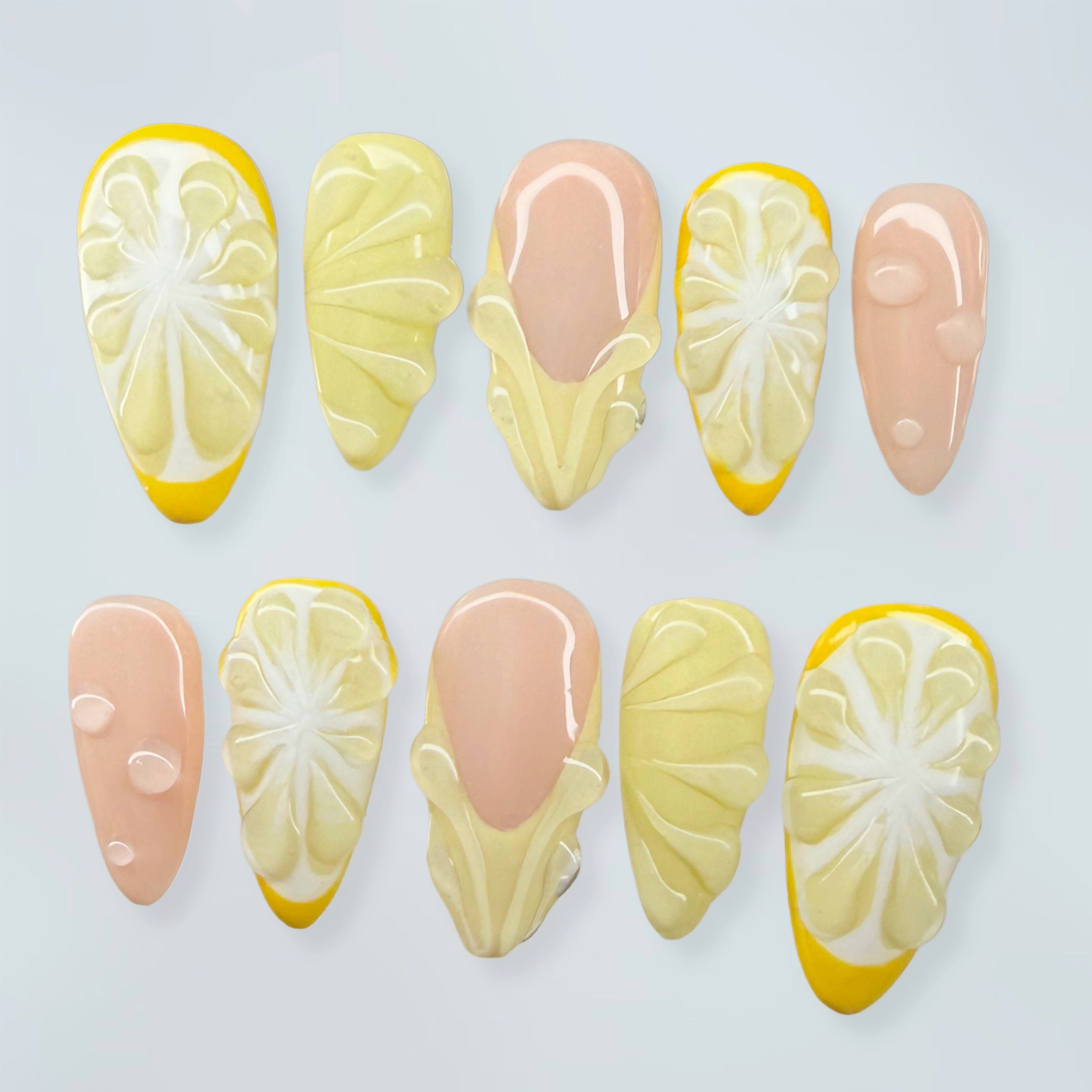 Nail art designs resembling lemon slices and pink bases on a light gray background