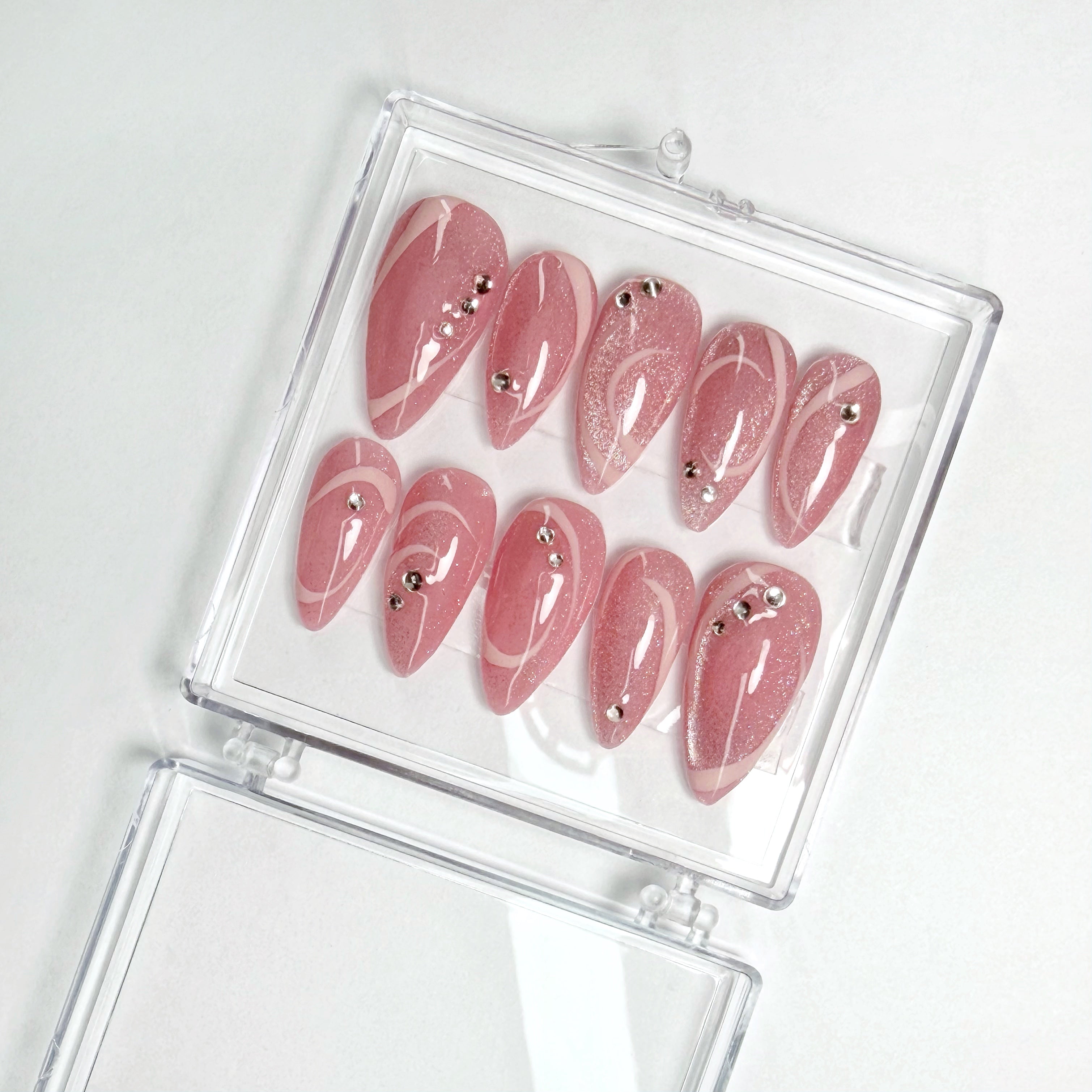 Set of pink nail extensions with rhinestones in a clear case on a white background