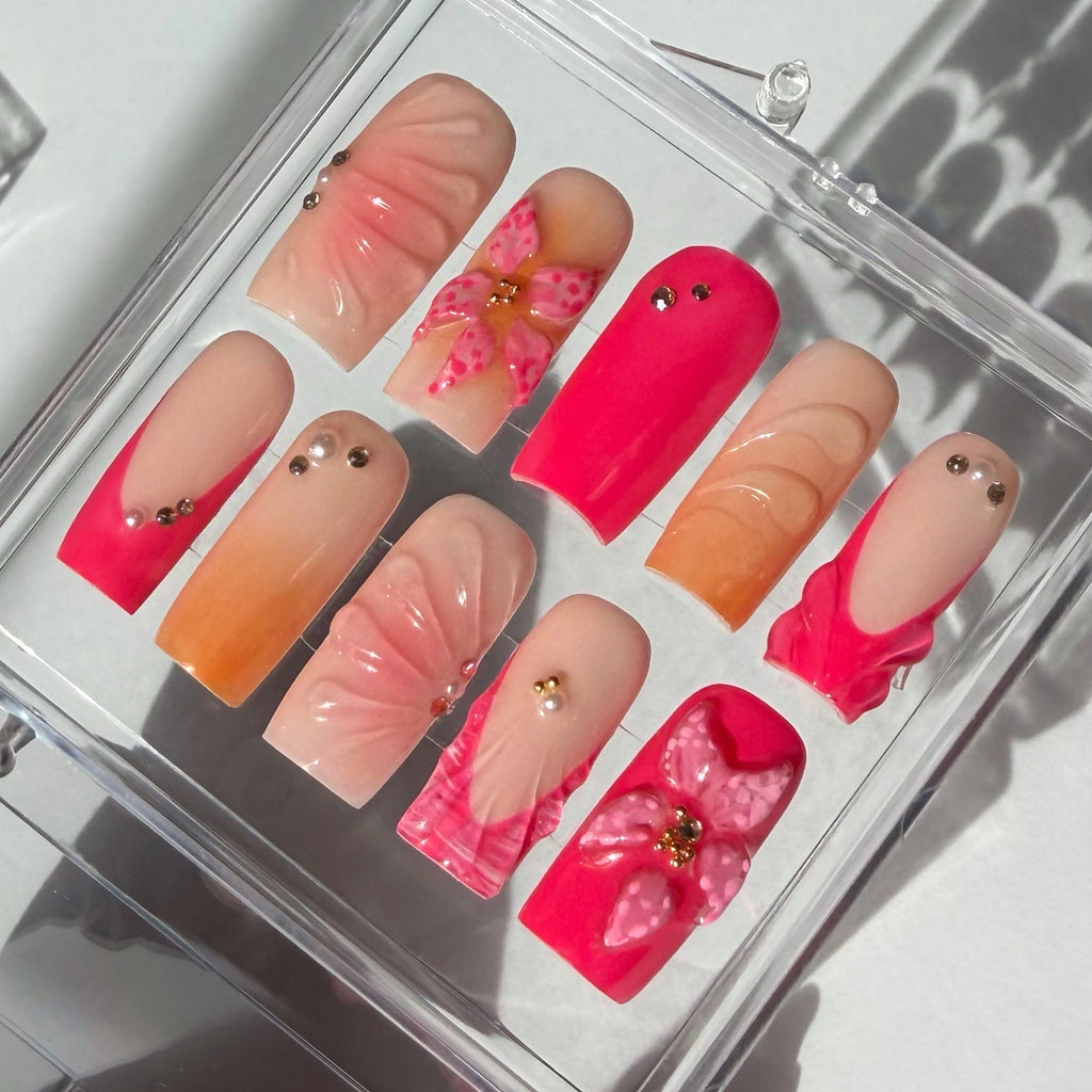 Set of pink and orange false nails with decorative elements in a clear display case.