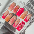 Set of pink and orange false nails with decorative elements in a clear display case.