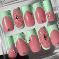 Set of pink and green gradient nails with decorative elements on a clear display.