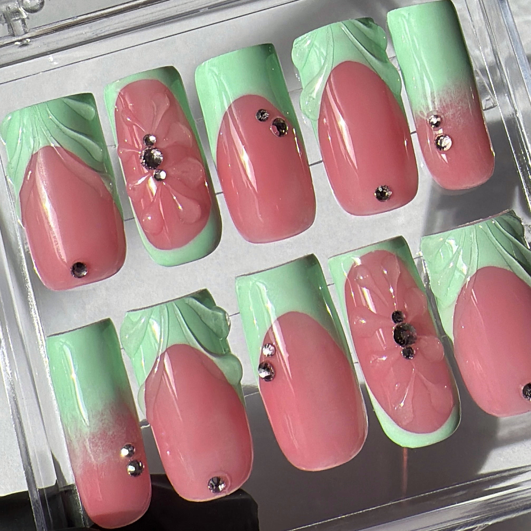 Set of pink and green gradient nails with decorative elements on a clear display.