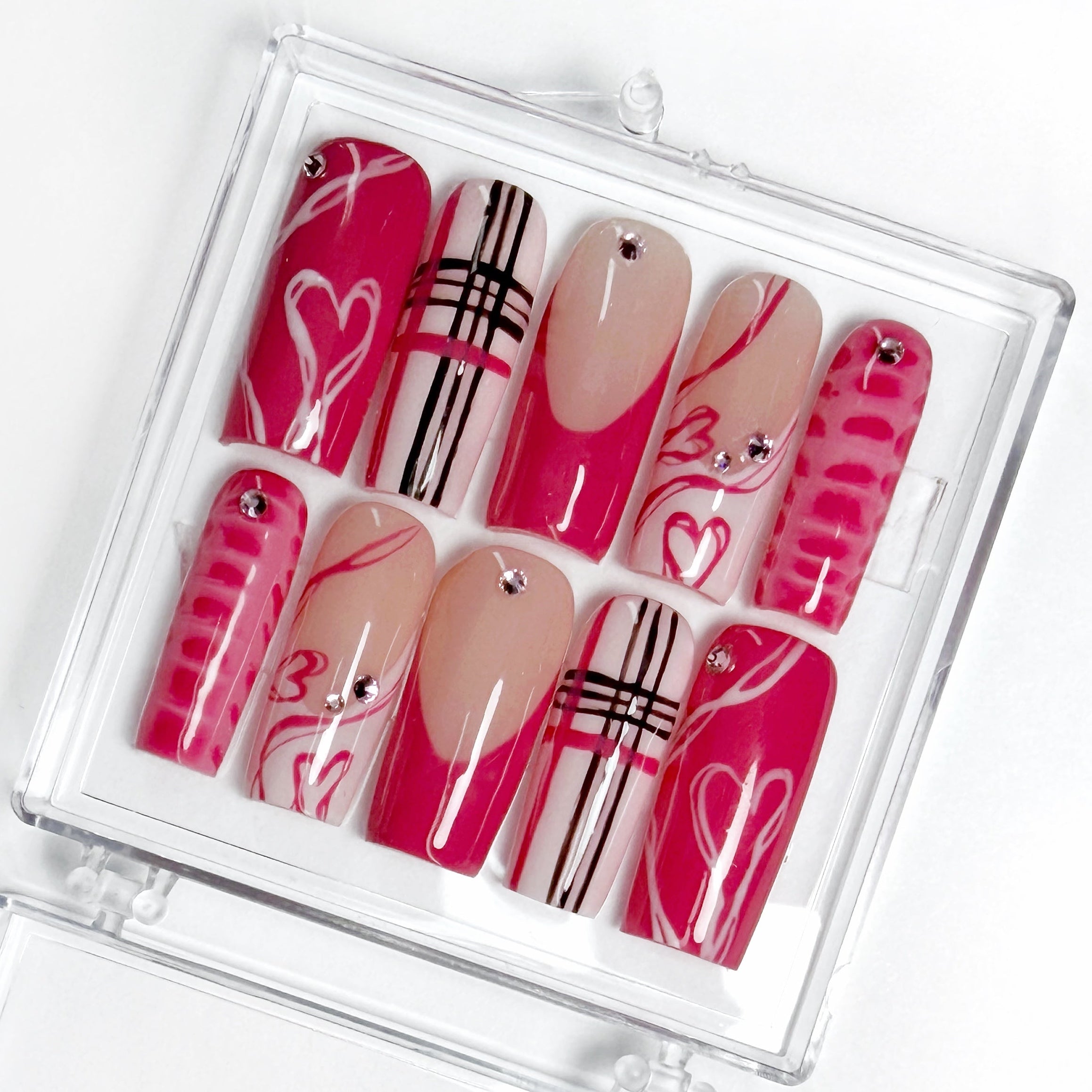 Set of decorative false nails pink with various hearts, French tips, crocodile print, in a clear case on a white background