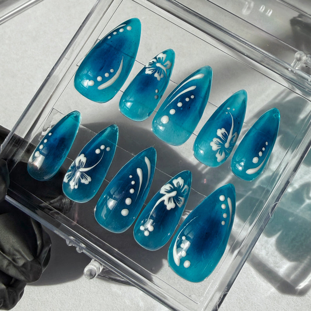 Set of blue nails with white flower nail art designs in a clear display case.