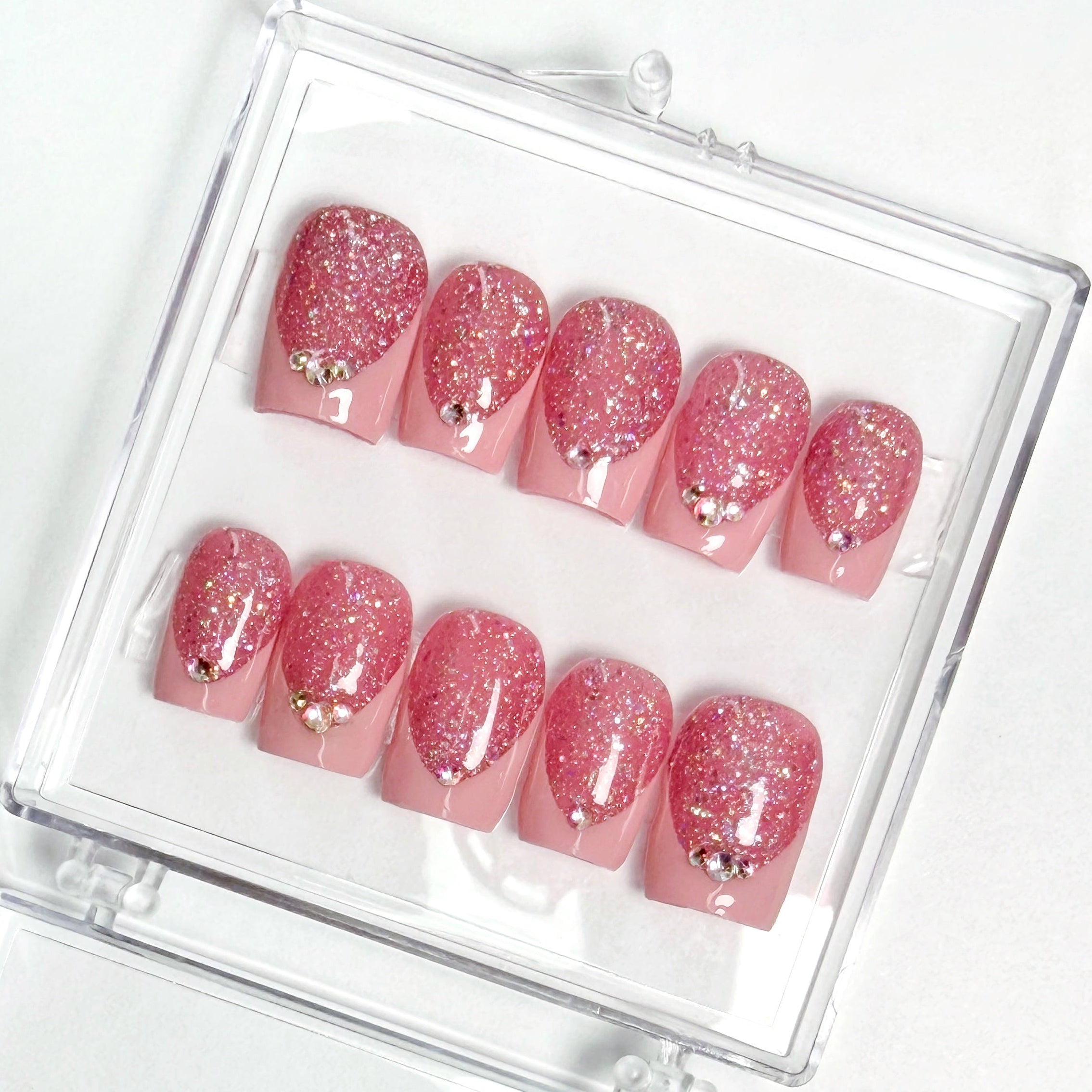 Set of pink glittery nails with gold accents in a clear case on a white background