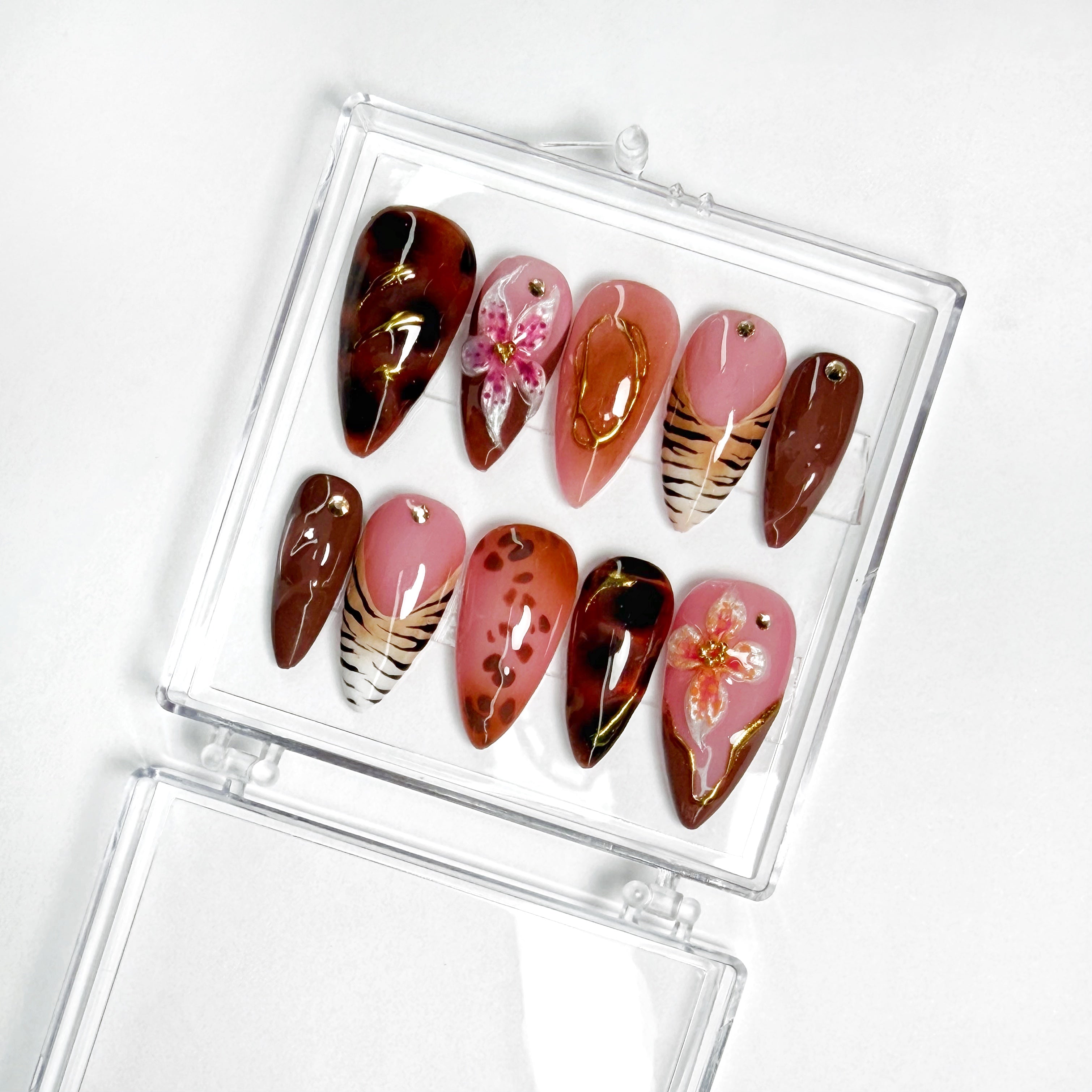 Pink and brown handmade press-on nail set with tortoiseshell, floral, and gold accent designs in a clear case on a white background.