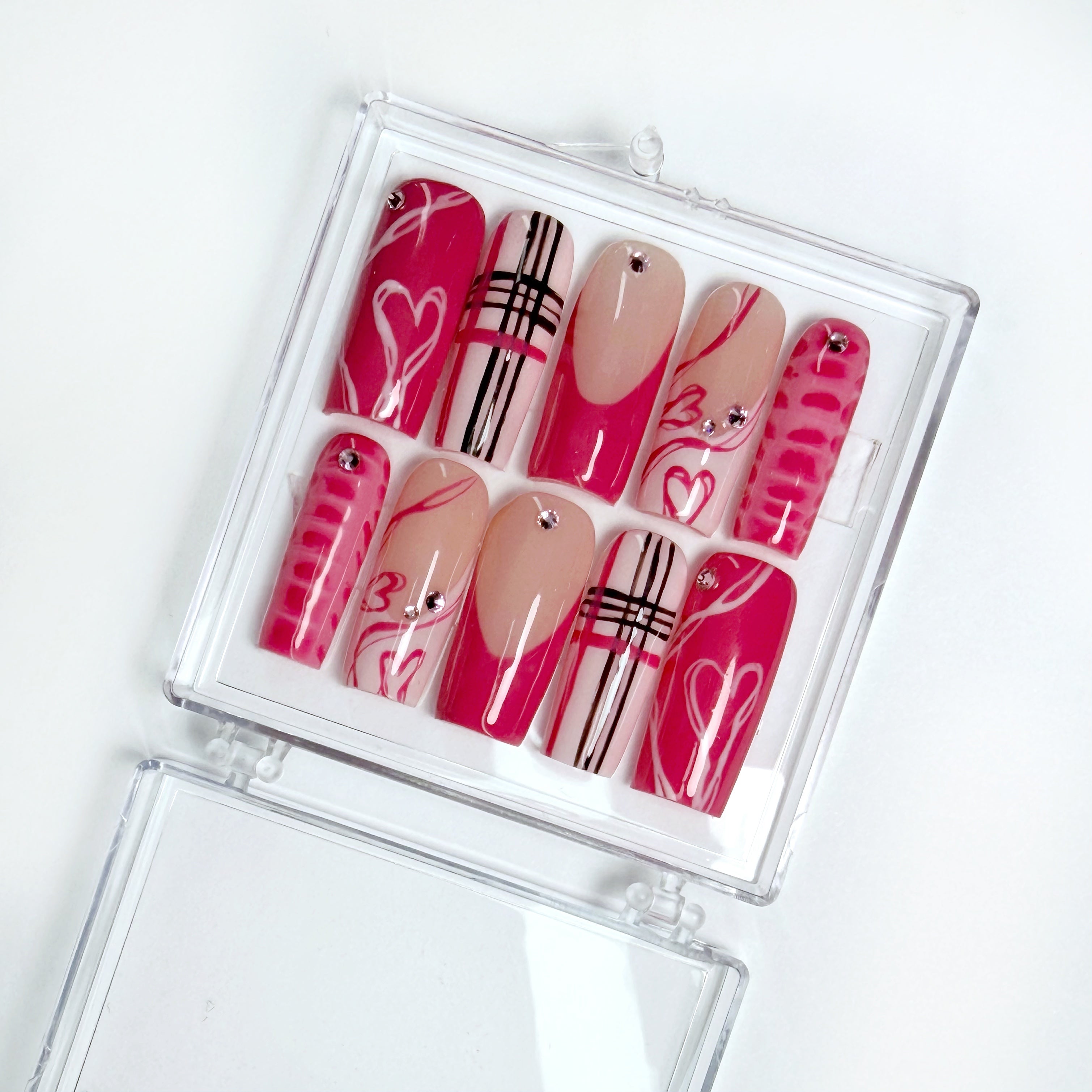 Set of decorative false nails in pink and beige with patterns in a clear case on a white background