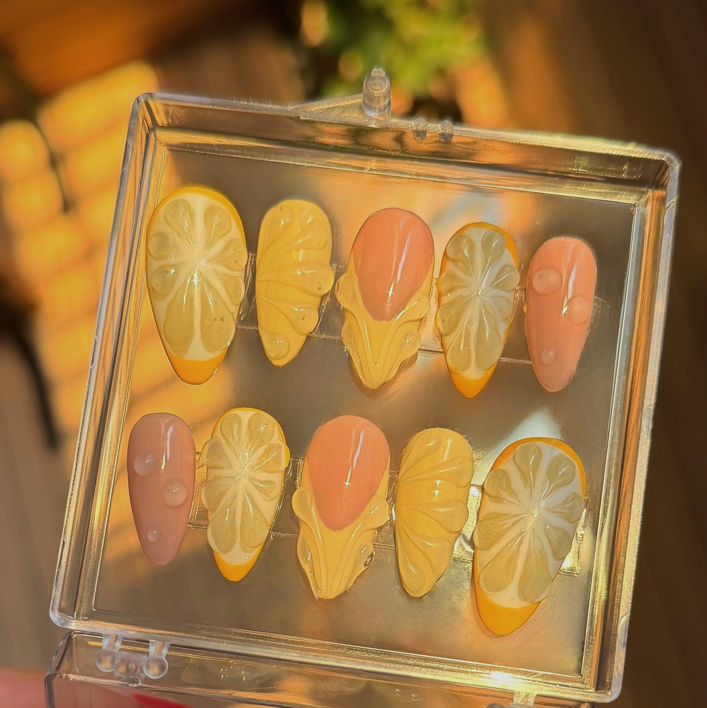 Set of nail art designs in a clear case, featuring lemon designs on almond nail shapes.