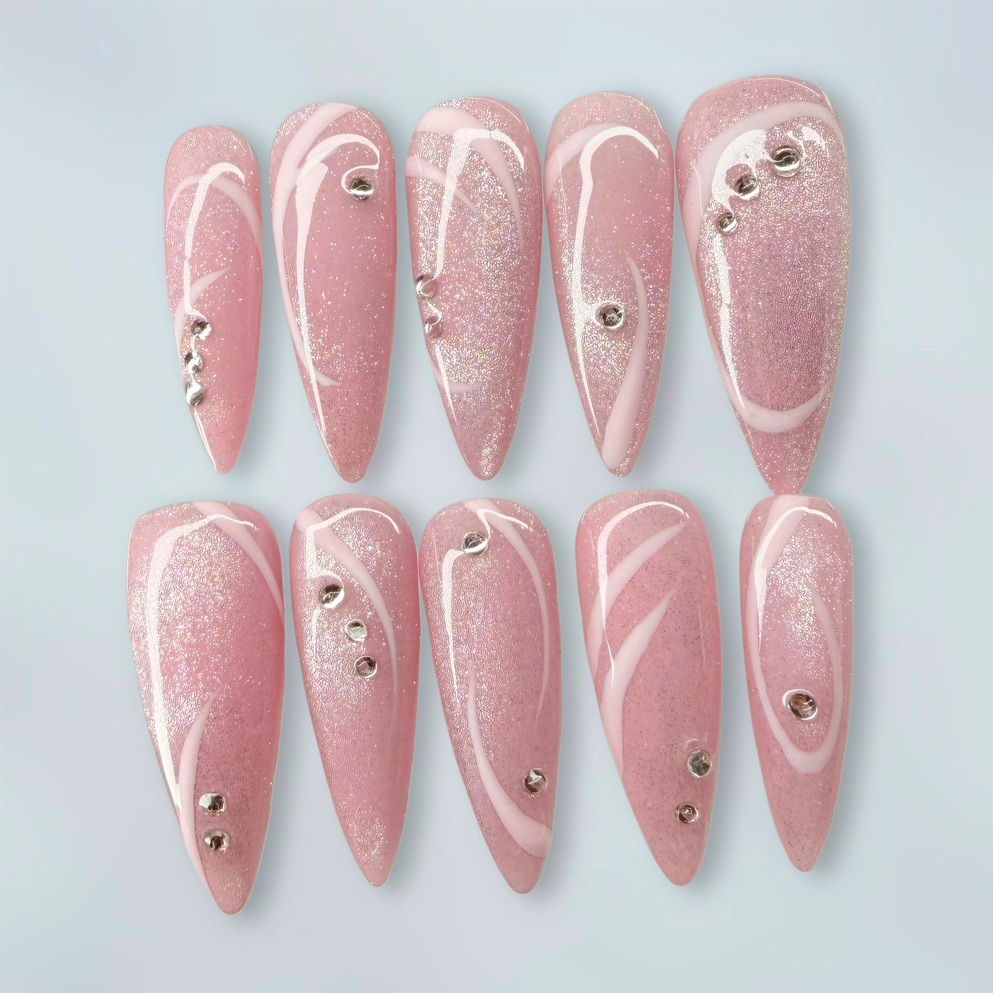 Set of pink cat eye glitter nail extensions with pink line patterns on a light gray background