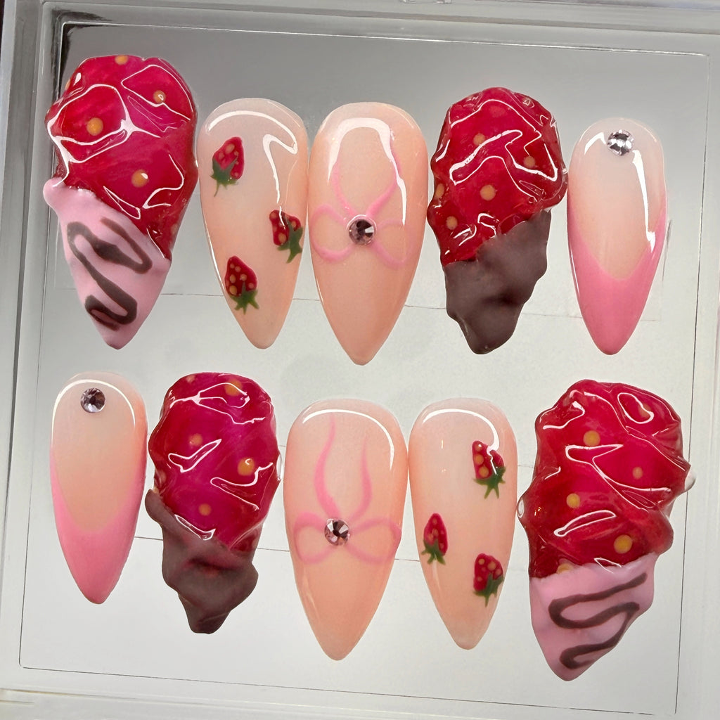 Artificial nails with bows and strawberry design on a white background. 4 of the 10 nails have a silver rhinestone.