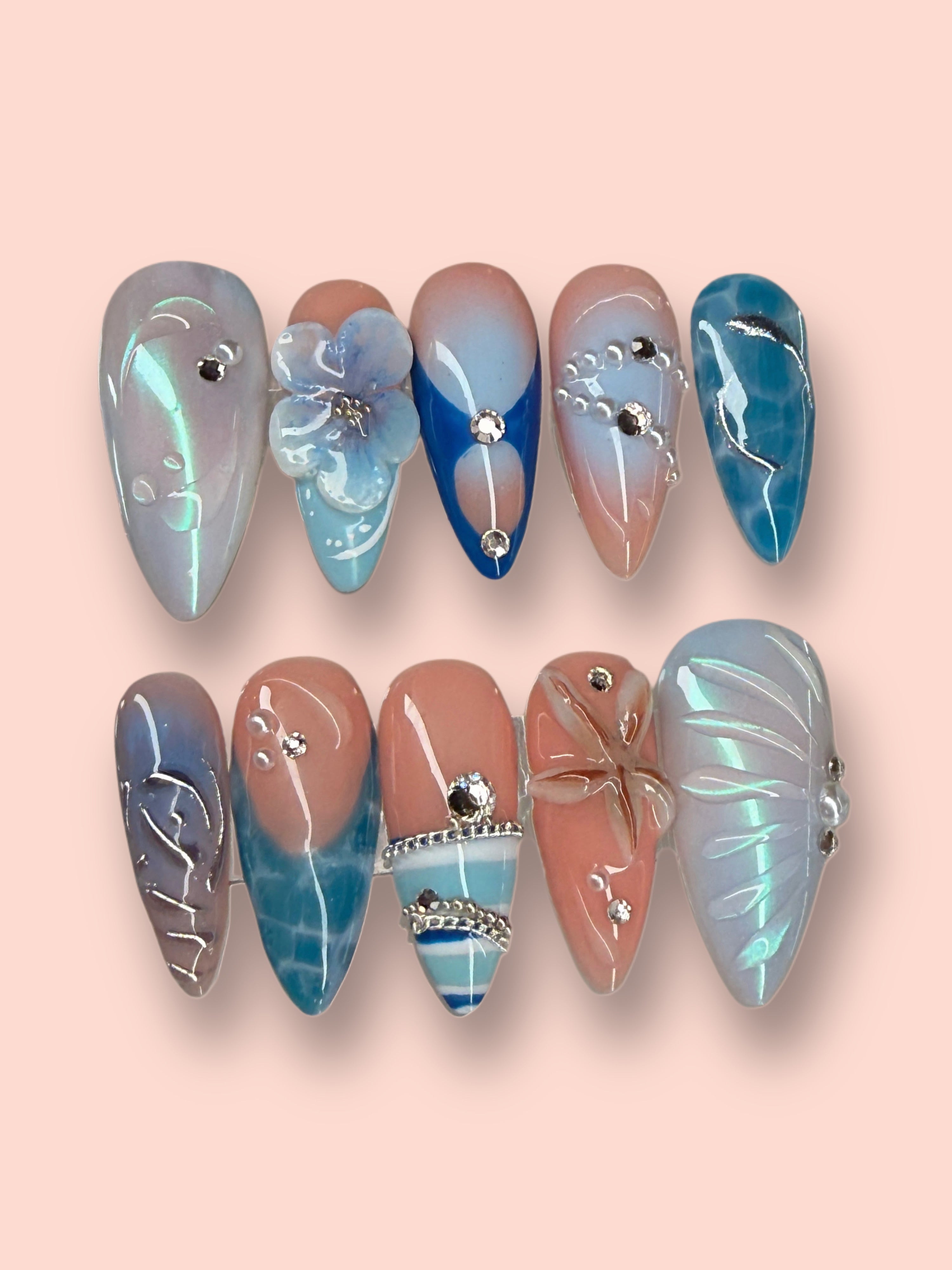 Set of decorative nails with blue, pink, and silver designs on a pink background