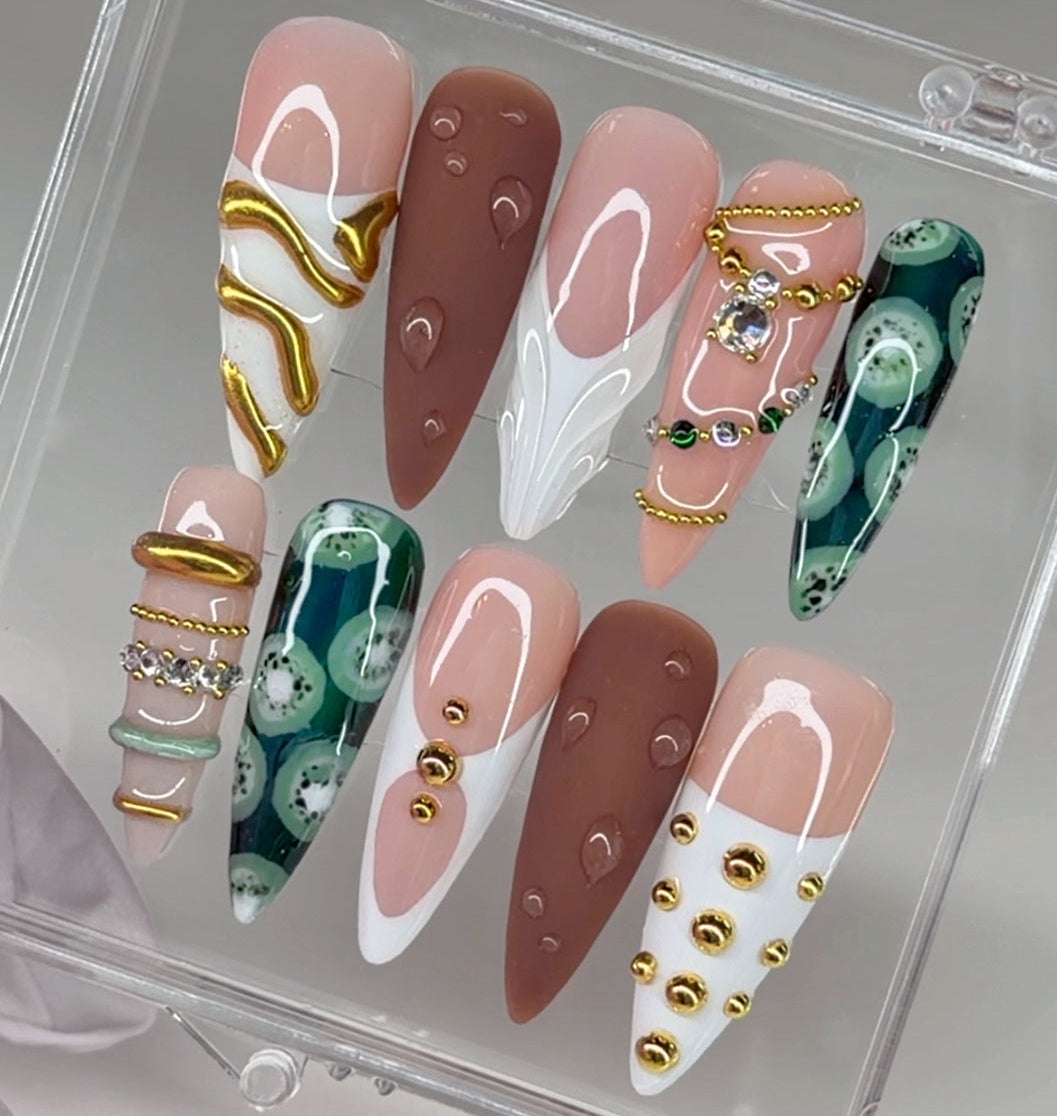 Set of decorative nails with various designs including gold, green, and white patterns.