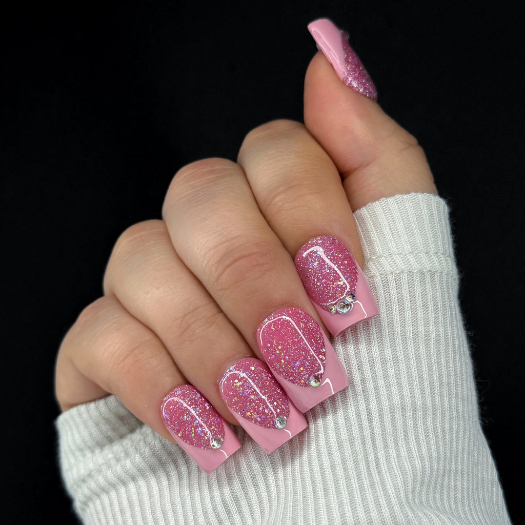 Hand with pink glittery nails and a white sleeve on a black background