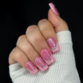 Hand with pink glittery nails and a white sleeve on a black background
