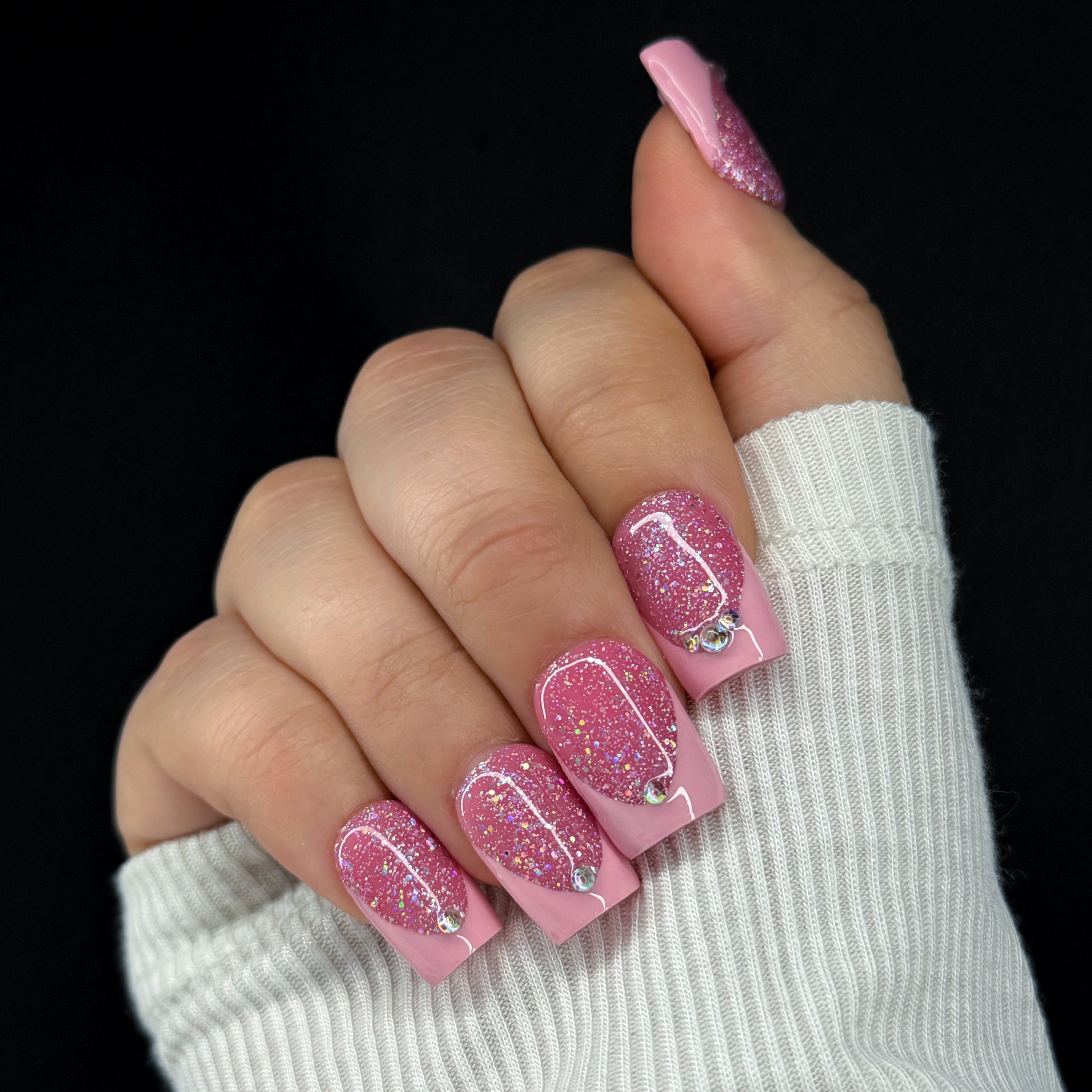 Hand with pink glittery nails and a white sleeve on a black background