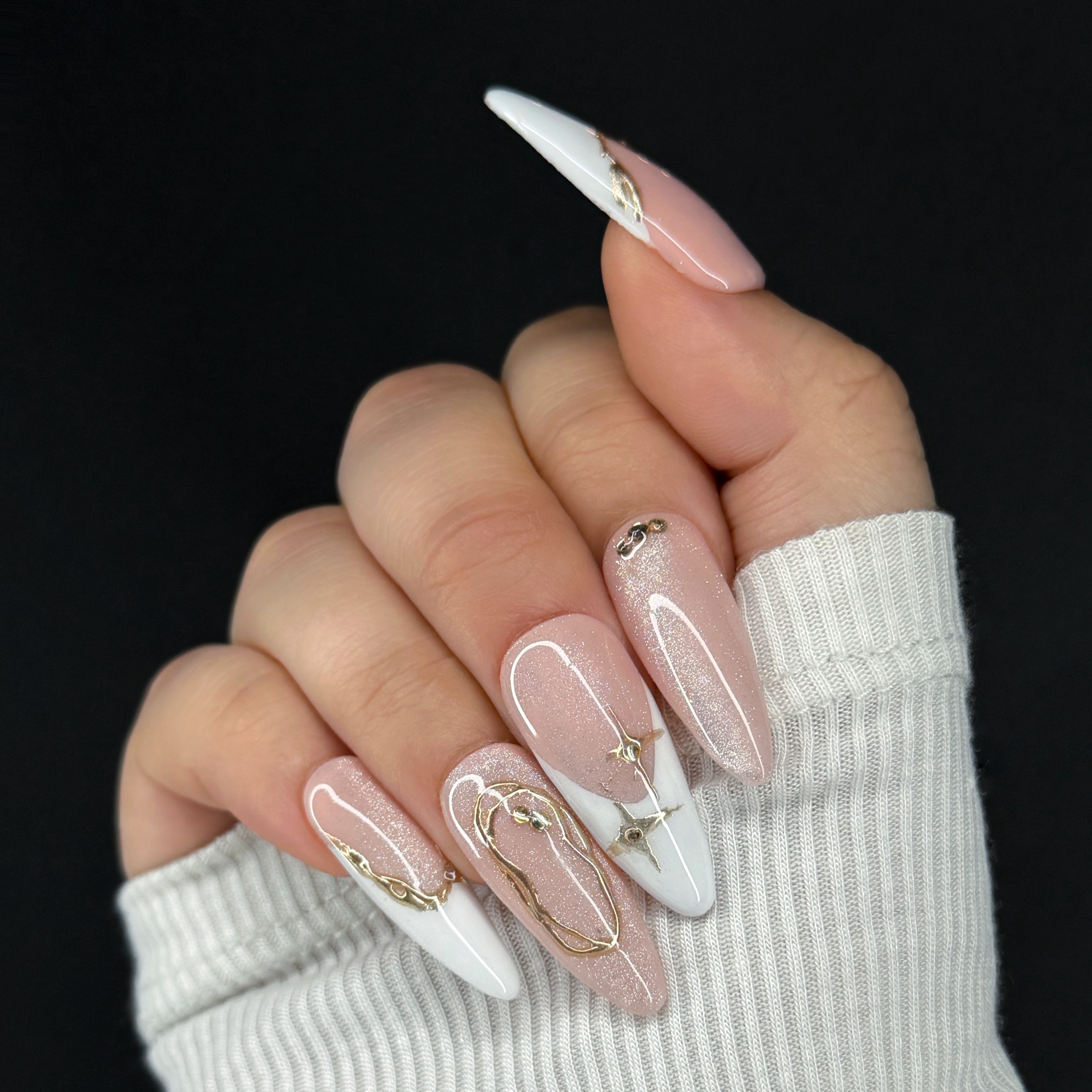 Hand with pink and white nails featuring gold accents against a black background